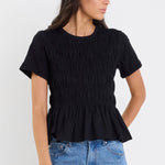 Woman wearing a black ruffled top and blue jeans against a white background