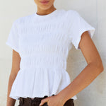 Woman wearing a white top and brown pants against a white background