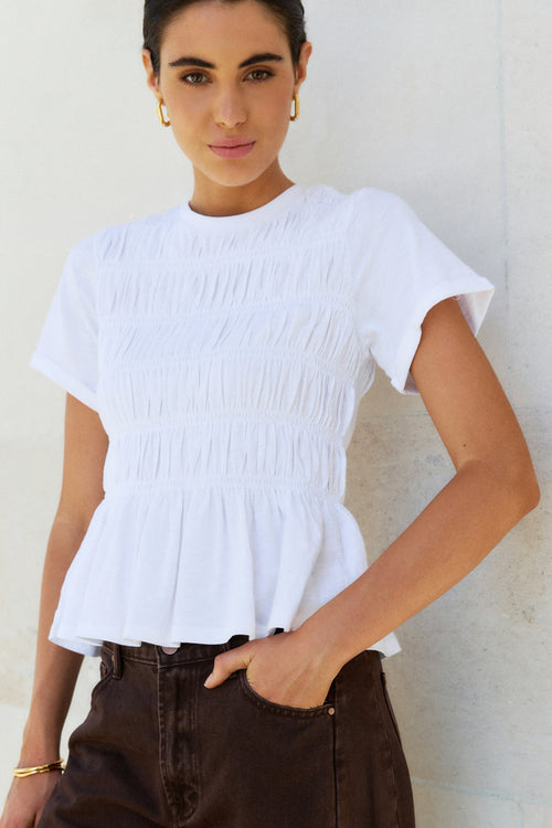 Woman wearing a white top and brown pants against a white background