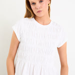 Model wearing a white short sleeve shirred cotton top with a peplum hem and crew neckline