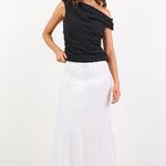 Woman wearing a black one-shoulder top and white pants on a white background