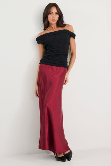 Woman wearing a black off-shoulder top and burgundy pants on a white background