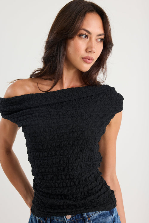 Woman wearing a black off-shoulder top against a white background