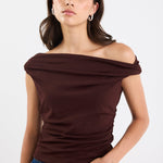 Woman wearing a brown off-shoulder top and blue jeans on a white background