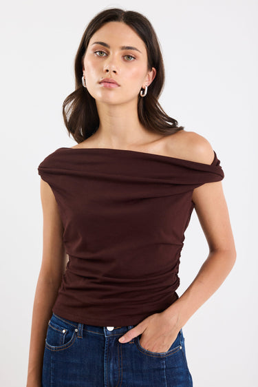 Woman wearing a brown off-shoulder top and blue jeans on a white background