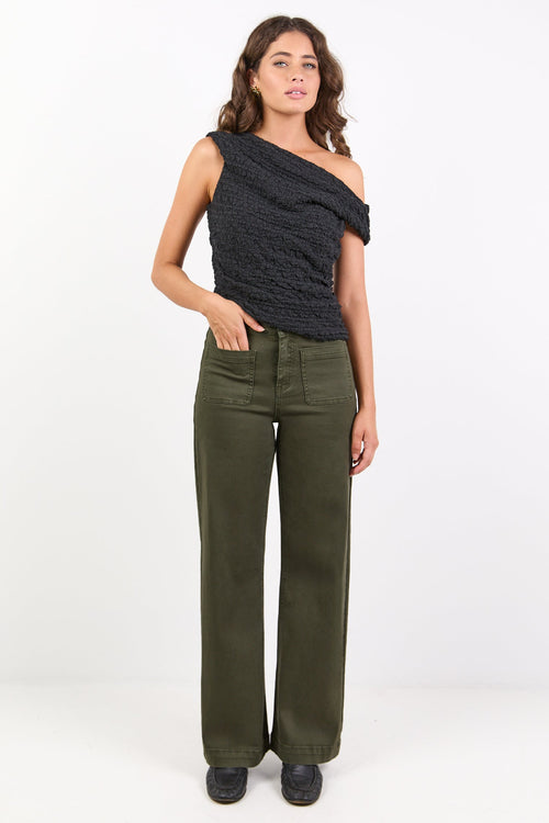 Woman wearing a black one-shoulder top and green pants on a white background