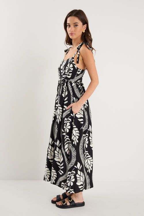 The model wears a black and white leaf print strappy maxi dress with black sandals