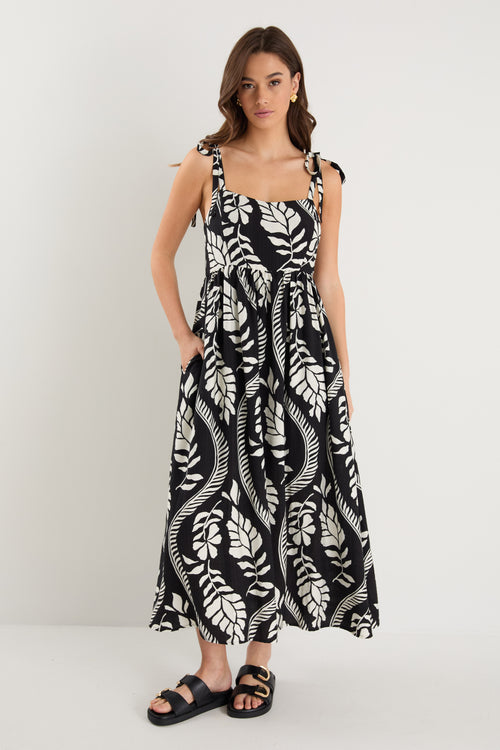 The model wears a black and white leaf print strappy maxi dress with black sandals
