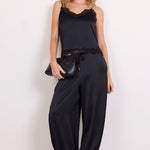 A woman modeling a black sleeveless camisole top with ruffled trim and matching black harem pants, styled with black sandals and sunglasses against a plain white studio background.