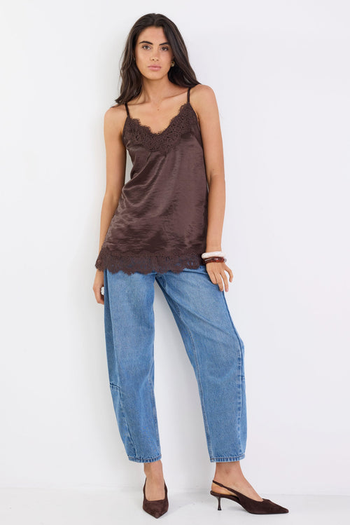 Woman wearing a brown satin camisole and blue jeans on a white background