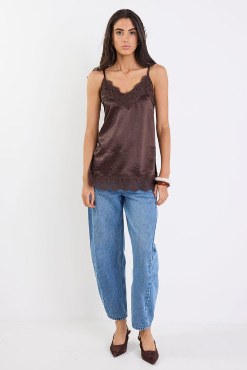 Woman wearing a brown satin camisole and blue jeans on a white background