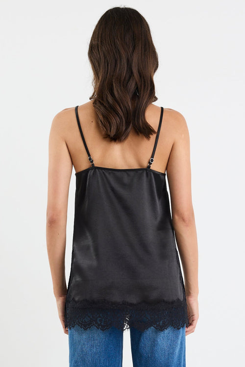 Woman wearing a black slip top and blue jeans on a white background