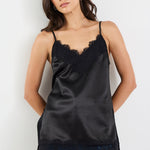 Woman wearing a black satin camisole with lace trim and blue jeans on a white background