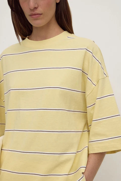A close-up of a model wearing an oversized pale yellow t-shirt with thin horizontal navy stripes.
