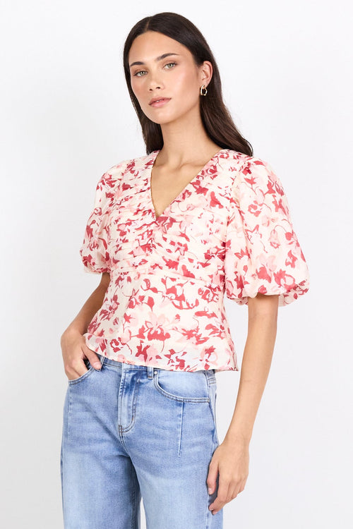 A woman modeling a short-sleeve floral blouse with puff sleeves and light-wash wide-leg cropped jeans, standing against a plain white studio background.