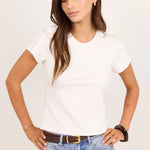 A woman modeling a fitted white short-sleeve crewneck t-shirt paired with light-wash blue jeans and a brown belt, standing against a plain off-white studio background.