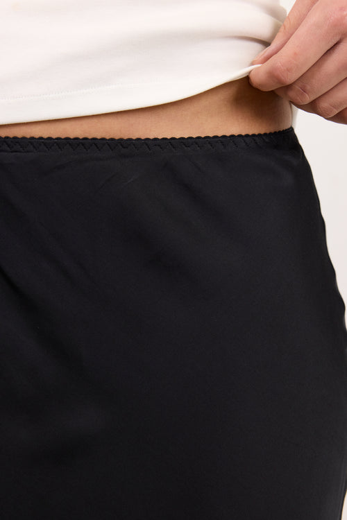 Close-up of a person wearing black bottoms with a white top, lifting the hem of the top to show the black waistband.