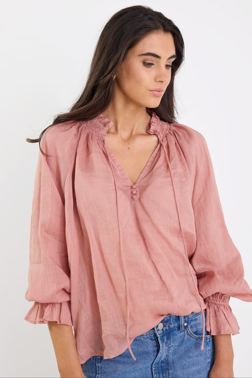Woman wearing a pink blouse with ruffled sleeves and blue jeans on a white background
