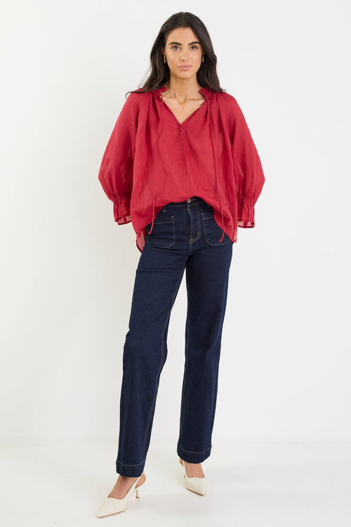 Woman wearing a red blouse and dark jeans on a white background