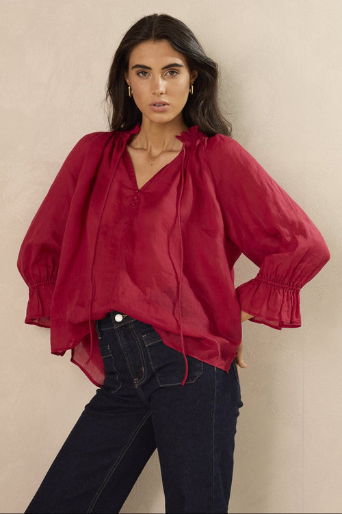 Woman wearing a red blouse with puffed sleeves against a beige background