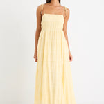 Woman wearing a pale yellow shirred maxi dress with thin tie-up straps and a flowing tiered skirt, paired with neutral sandals.