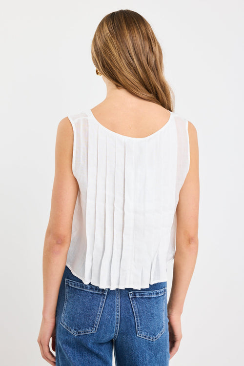 Woman wearing an ivory pleated sleeveless top with tie neckline, styled with high-waisted blue jeans.