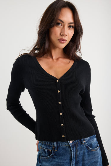 Woman wearing a black cardigan with gold buttons on a white background