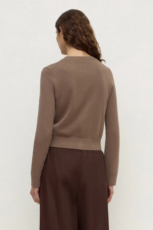 A woman shown from the back wearing a cropped, long-sleeve knit sweater in taupe brown and dark brown wide-leg trousers, set against a plain off-white studio background.