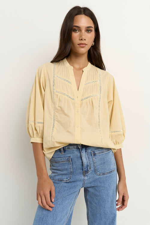 Woman wearing a soft yellow cotton blouse with pintuck and ladder lace details, styled with light blue wide-leg jeans.
