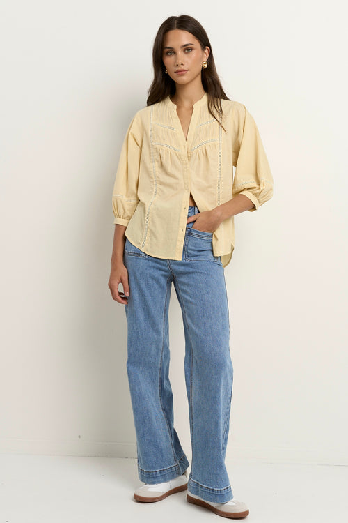 Woman wearing a soft yellow cotton blouse with pintuck and ladder lace details, styled with light blue wide-leg jeans.
