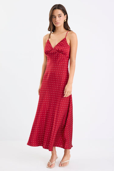 Woman wearing a red satin midi dress with white polka dots, adjustable spaghetti straps, and a bias-cut silhouette, standing against a white background.