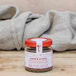 Jar of 'sweet & smoky' seasoning on a wooden surface with a beige blanket in the background