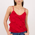 A woman modeling a red ruffled spaghetti-strap camisole top paired with blue jeans, set against a plain light background.