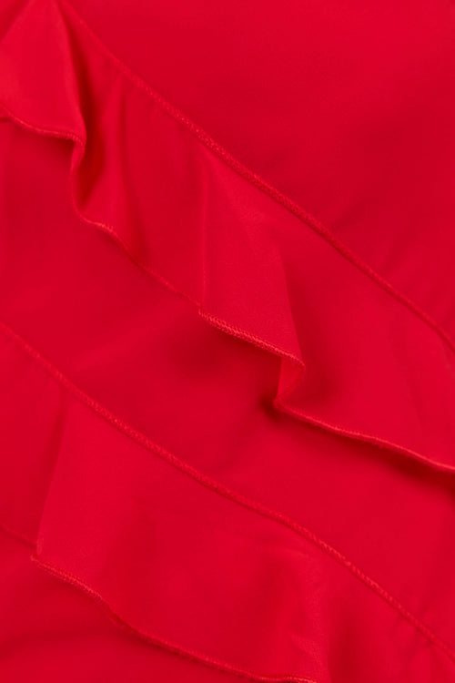 Close-up of a bright red ruffled garment fabric, showing layered diagonal ruffles and smooth satin-like texture.