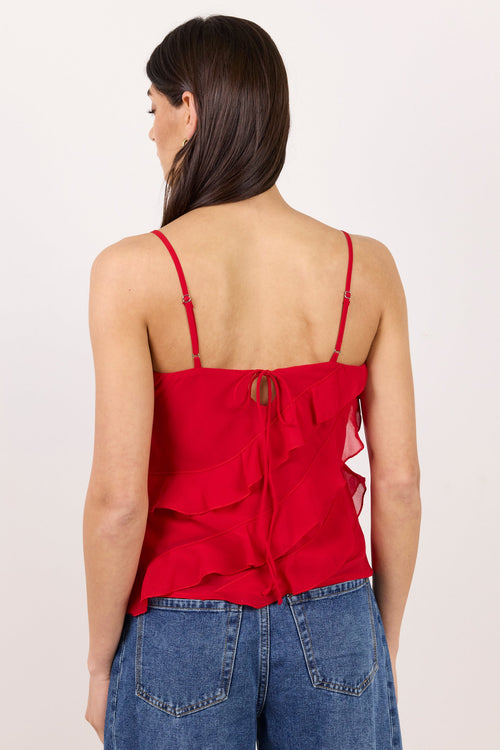 A woman shown from the back wearing a bright red spaghetti-strap ruffled camisole top and blue jeans against a plain off-white studio background.