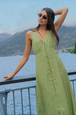 Woman in a green dress standing by a lake with mountains in the background