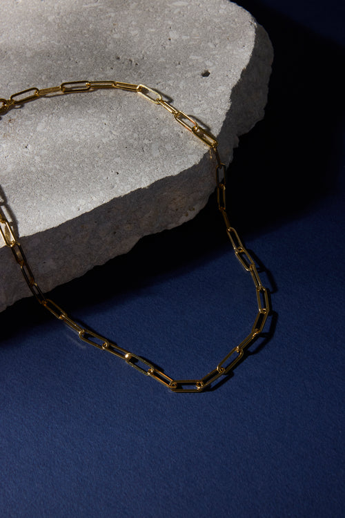 Gold chain necklace on a stone surface with a dark background