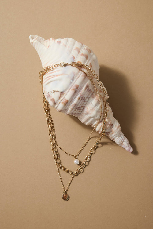 Gold triple-layer necklace with mixed chains, a pearl accent, and a round gold disc charm