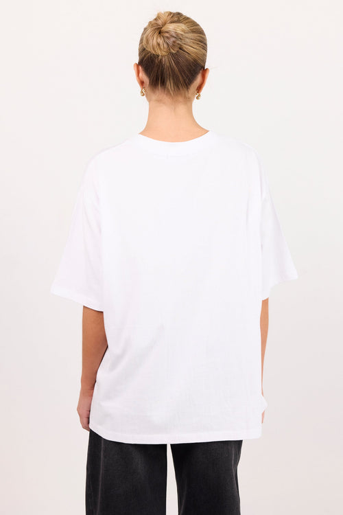 A person viewed from the back wearing an oversized white short-sleeve T-shirt and dark pants against a plain light background.