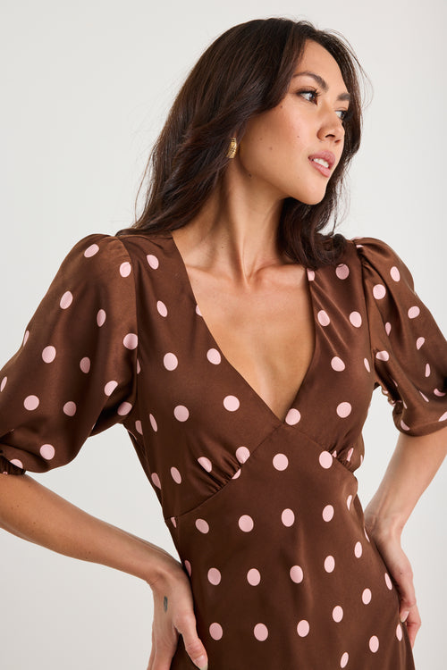 Woman wearing a brown dress with pink polka dots against a white background