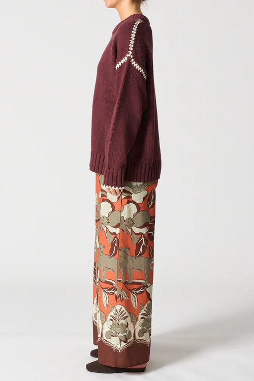 Person wearing a burgundy sweater and patterned pants on a white background
