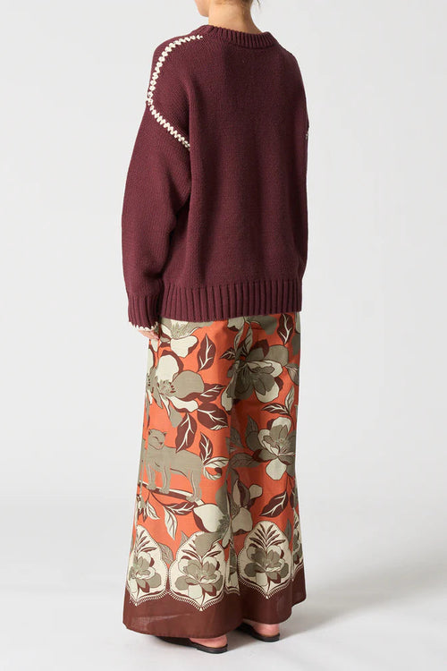 Person wearing a maroon sweater and floral-patterned pants on a white background