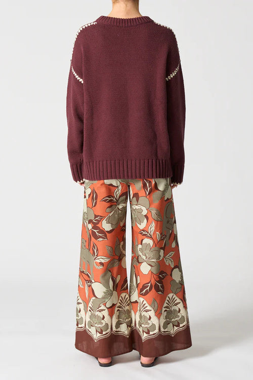 Person wearing a maroon sweater and floral-patterned pants on a white background