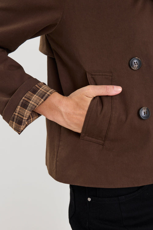 Close-up of a person wearing a brown jacket with plaid cuffs and button details.