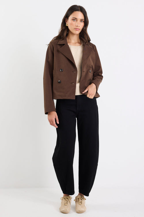 Woman wearing a brown jacket and black pants on a white background