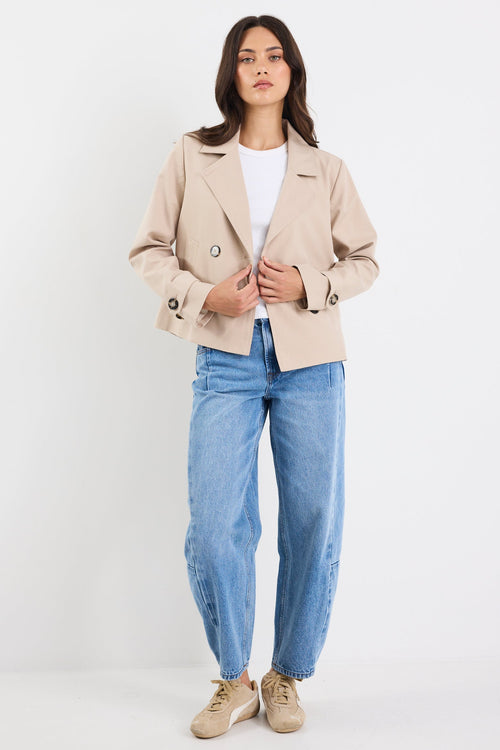Woman wearing a beige blazer, white shirt, blue jeans, and beige shoes on a white background