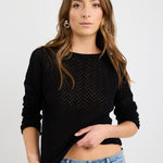 Woman wearing a black crochet knit boat neck jumper with long sleeves, styled with a light denim mini skirt.