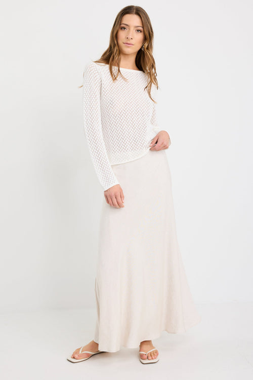 Woman wearing an ivory crochet knit jumper with boat neckline and long sleeves, styled with a natural skirt.