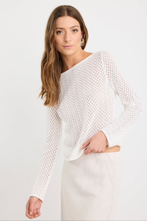 Woman wearing an ivory crochet knit jumper with boat neckline and long sleeves, styled with a natural skirt.