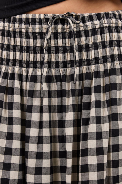 Close-up of a person wearing black and off-white gingham check wide-leg pants with a smocked elastic waist and drawstring.